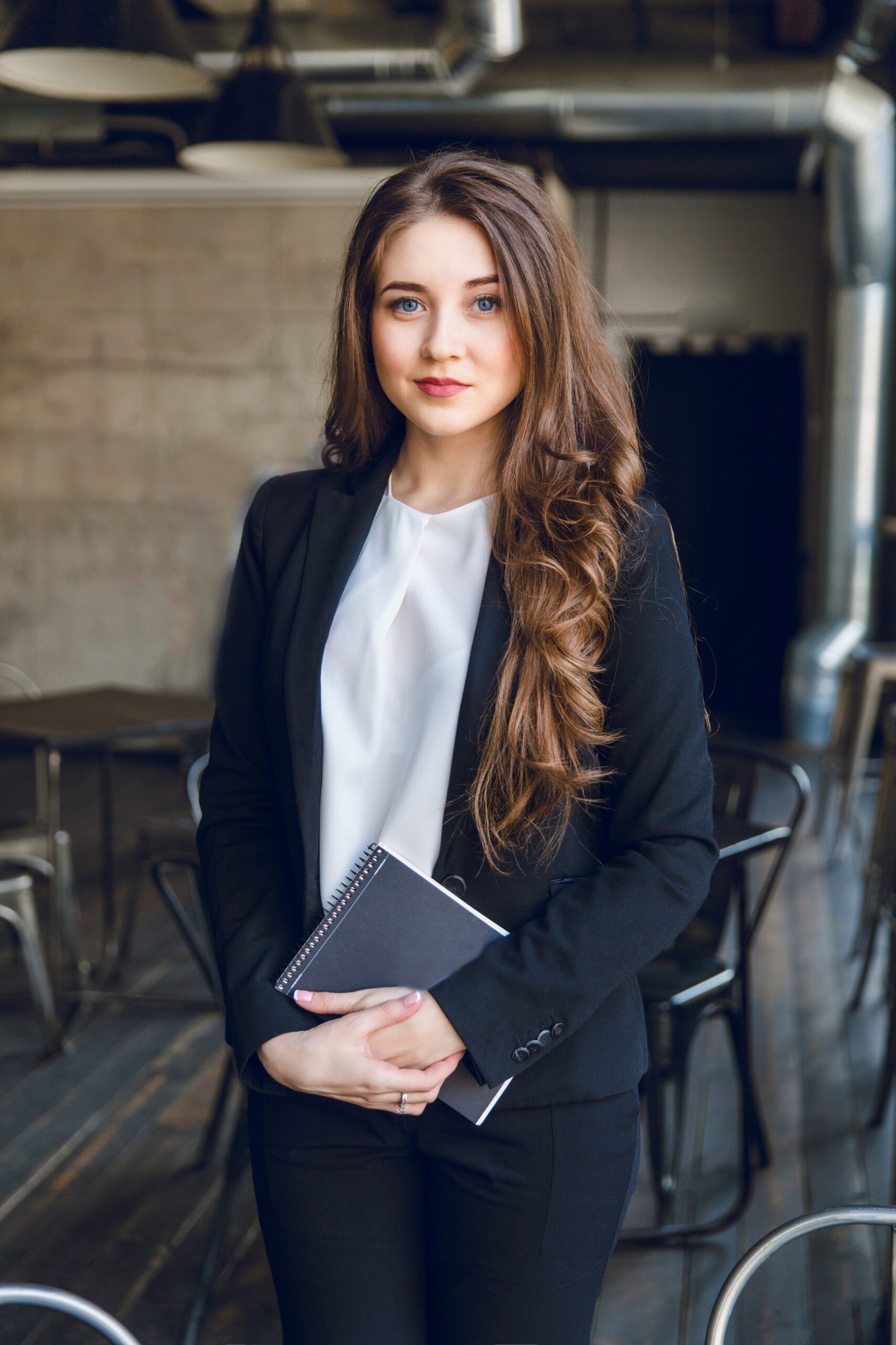 brunette-business-woman-with-wavy-long-hair-blue-eyes-stands-holding-notebook-hands