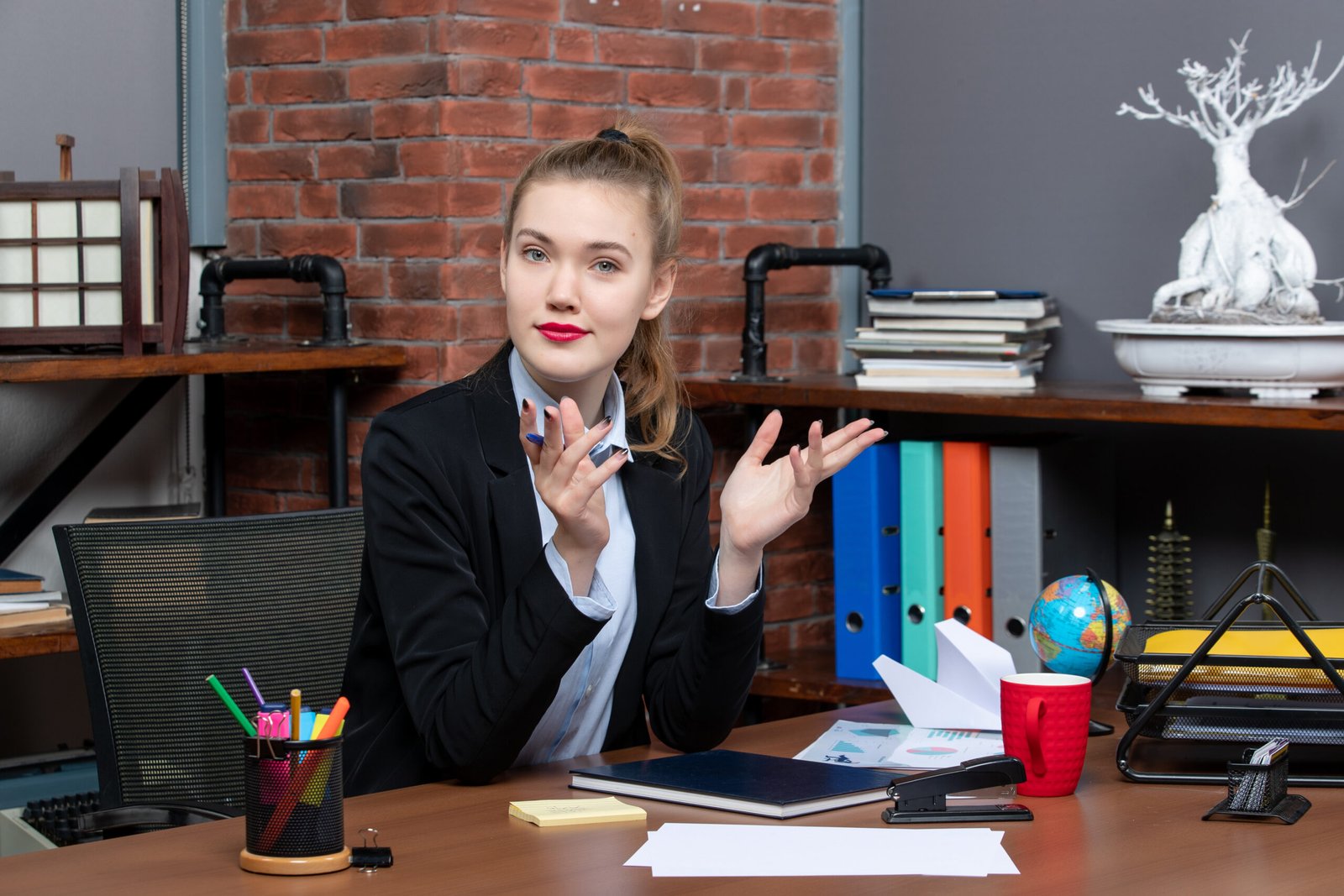 top-view-young-curious-female-office-worker-sitting-her-desk-posing-camera